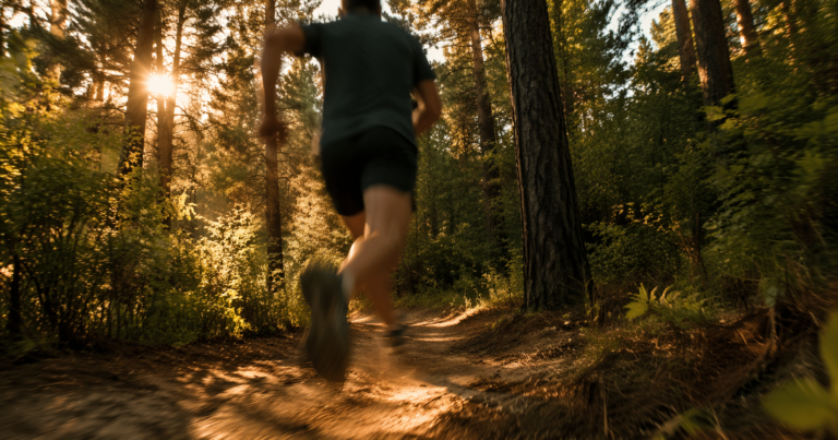Lone runner sprinting along a winding forest trail at golden hour, viewed from a low angle with motion blur, warm sunlight filtering through pine trees.